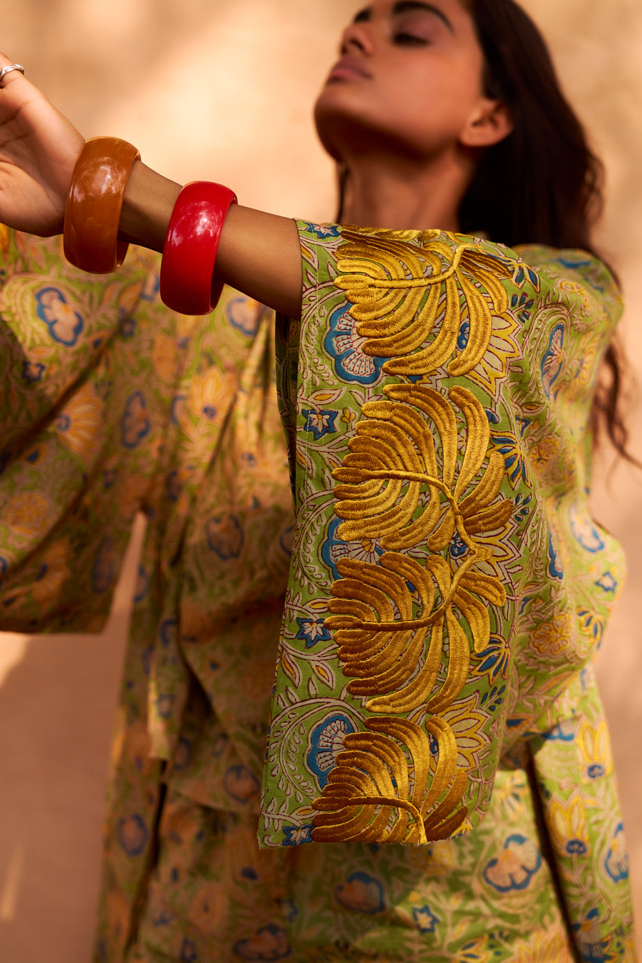 Model wearing the Kleed Jasmine Kimono in olive yellow with hand block printed feather motifs, styled with a red bangle