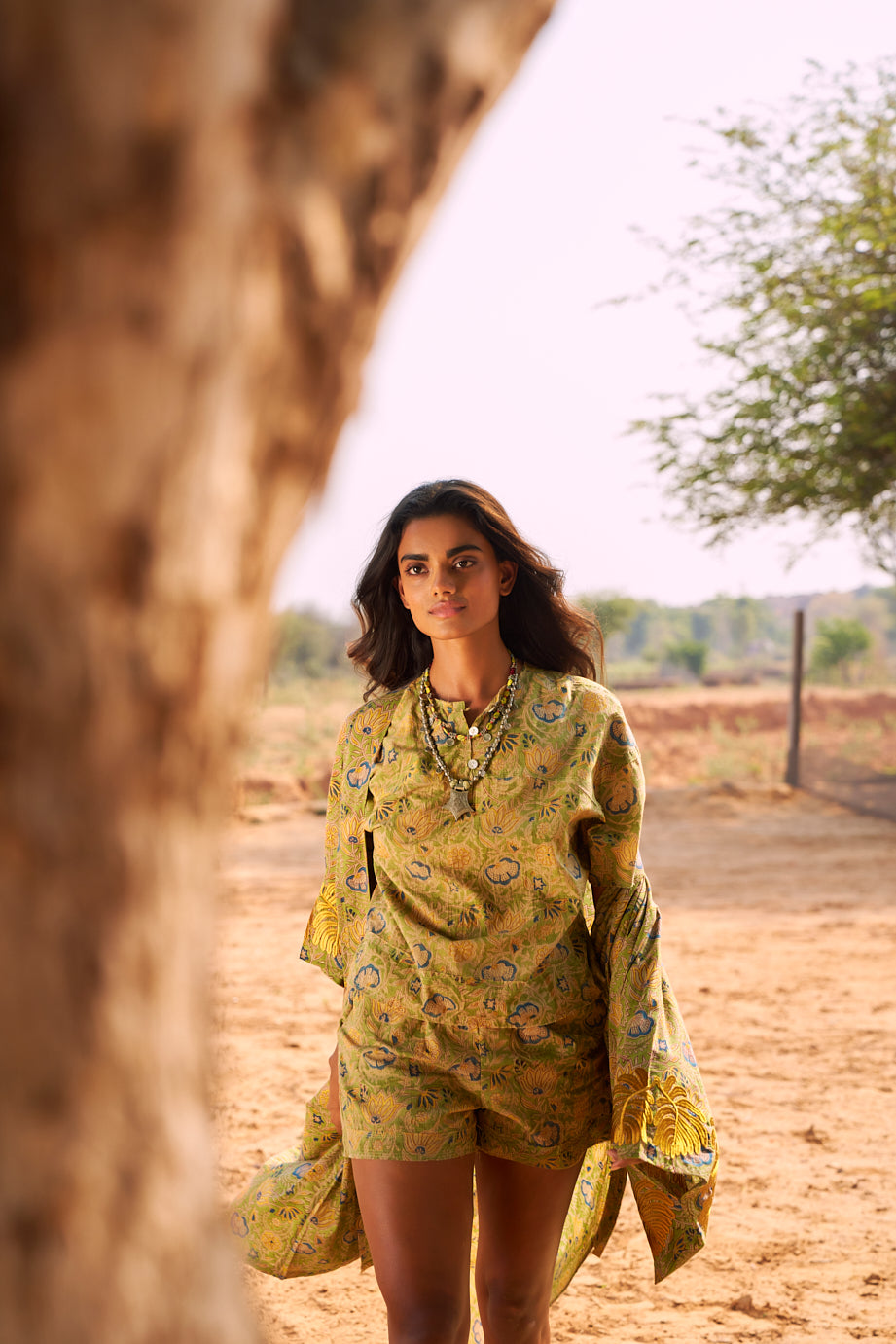The Kleed Jasmine Kimono photographed in movement, showing the fluid silhouette of the handcrafted cotton kimono next to a tree. Model wearing a matching jasmine mogra pyjama and boho necklaces.