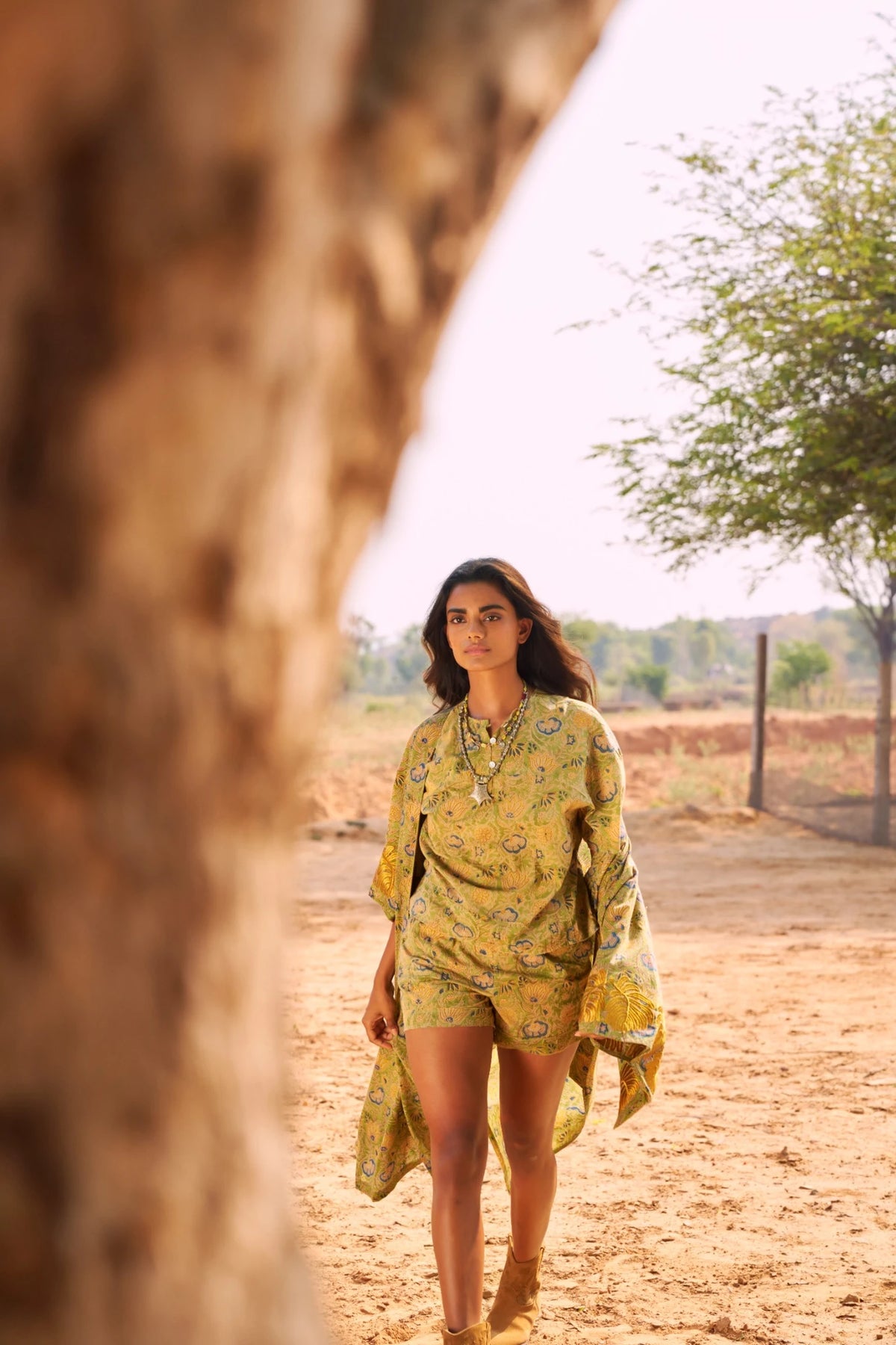 Kaner Jasmine Pyjama by KLEED, styled on a model walking outdoors in a sunlit natural landscape, wearing a green floral cotton pyjama set with matching shorts and kimono.