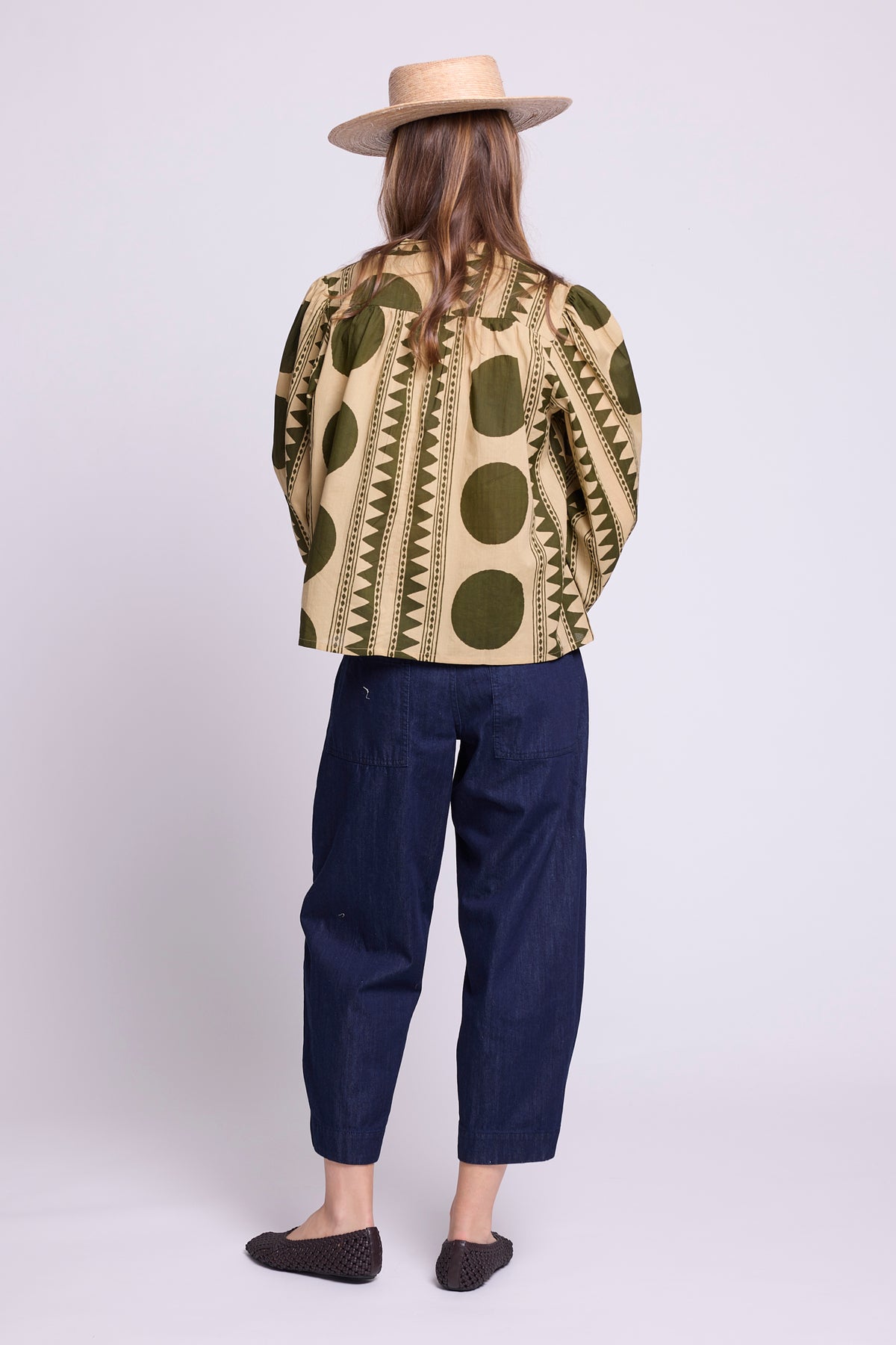 Model wearing the KLEED Khaki Geo Balloon Shirt in 100% cotton, back view styled with dark blue cropped trousers and a straw hat.