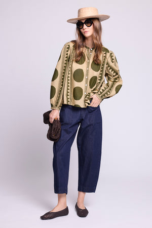 Model wearing the KLEED Khaki Geo Balloon Shirt in 100% cotton, styled with dark blue wide-leg trousers, straw hat and sunglasses.