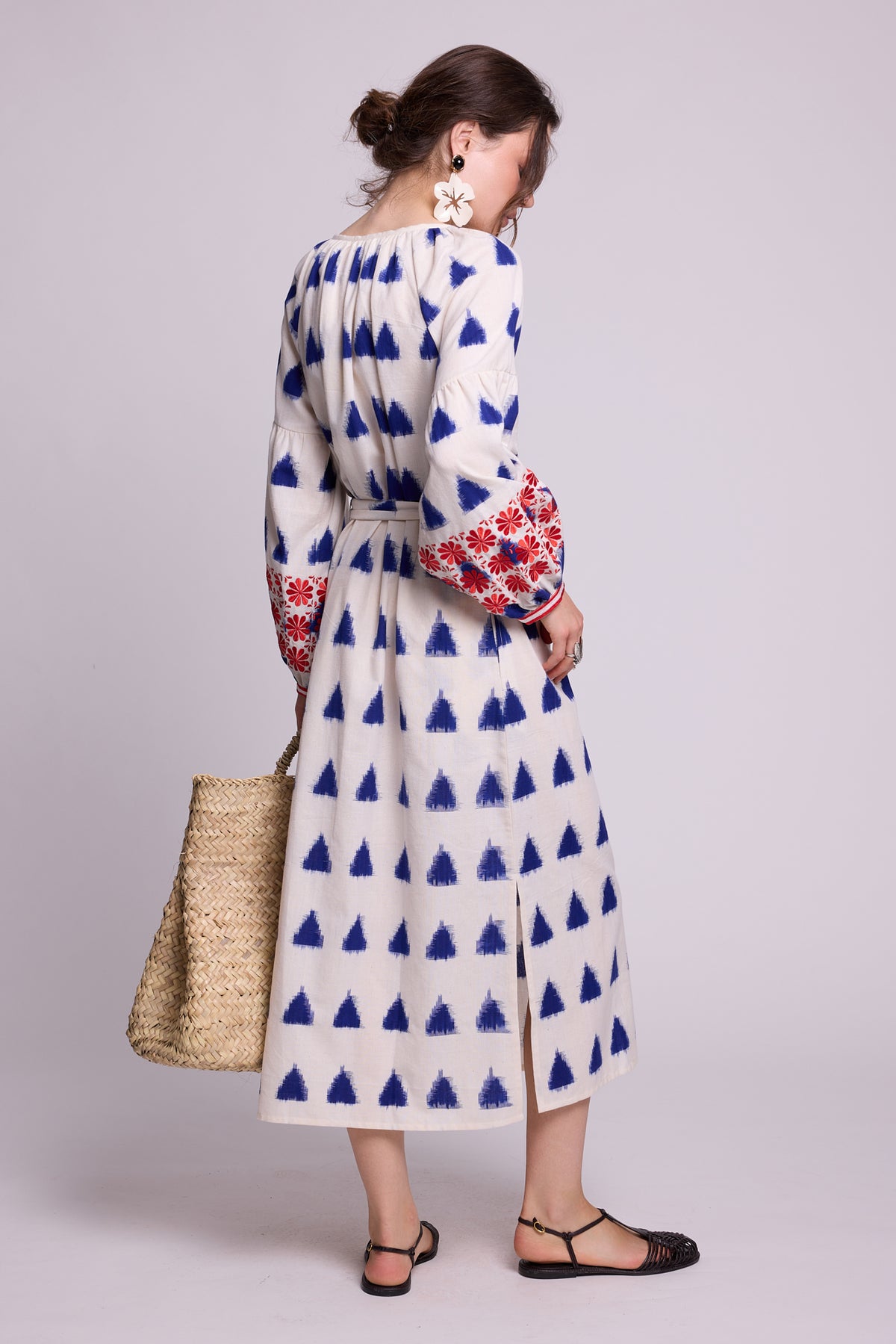 Side view of model wearing the KLEED Saint Tropez cotton-linen Kaftan with blue geometric print and red and blue embroidery, carrying a woven straw basket and wearing statement earrings and black sandals.