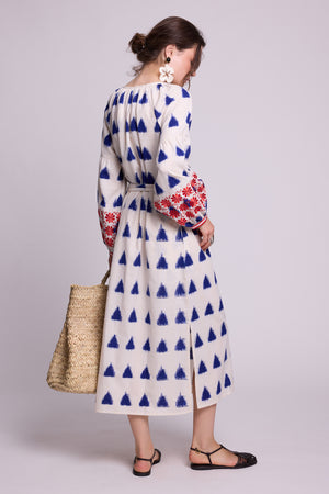 Side view of model wearing the KLEED Saint Tropez cotton-linen Kaftan with blue geometric print and red and blue embroidery, carrying a woven straw basket and wearing statement earrings and black sandals.
