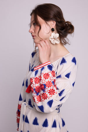 Close-up of model wearing the KLEED Saint Tropez Kaftan in cotton linen, showing the blue geometric pattern, red and blue embroidered sleeves, neckline details and statement earrings.