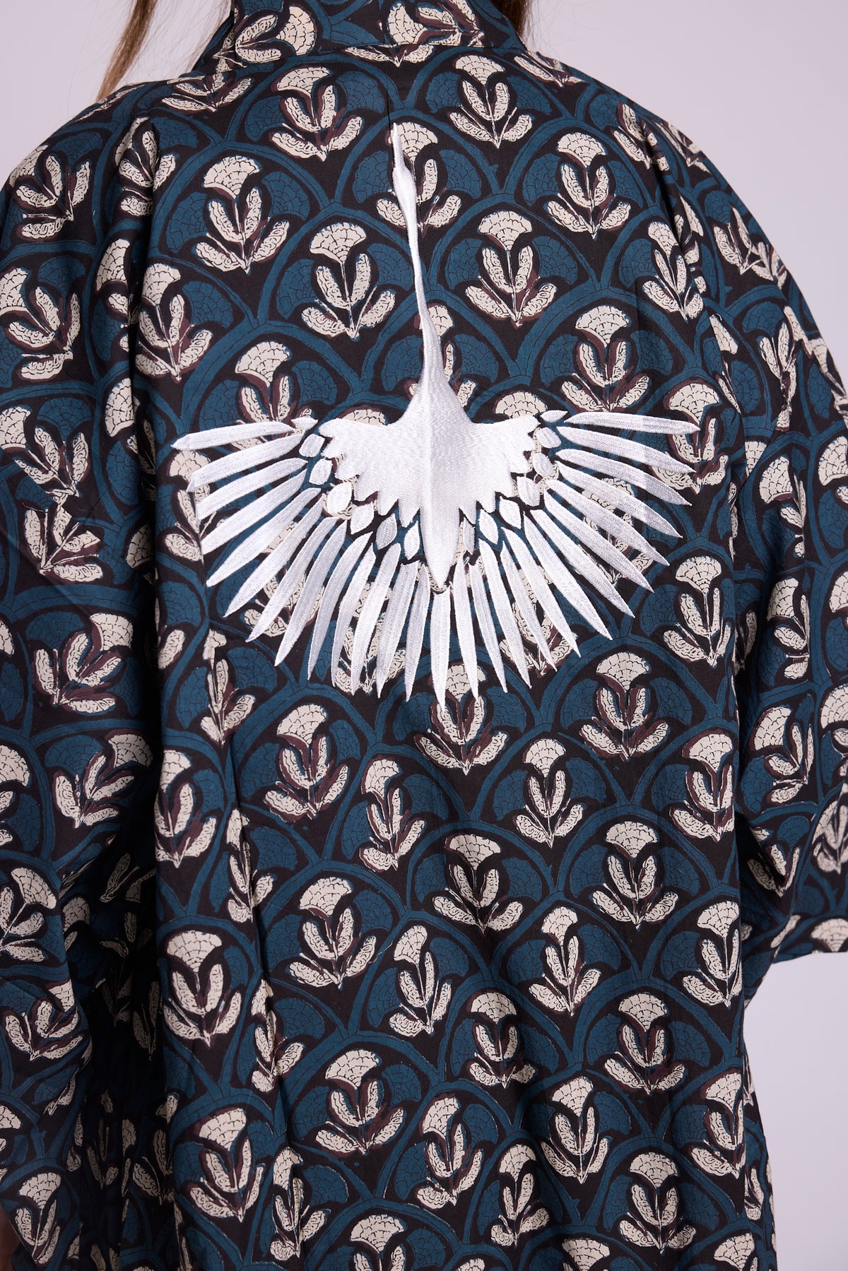 Close up of krisant naya kimono, from Kleed in 100% hand block printed cotton. Black with blue and white flower motifs. Embroidered crane at the back.