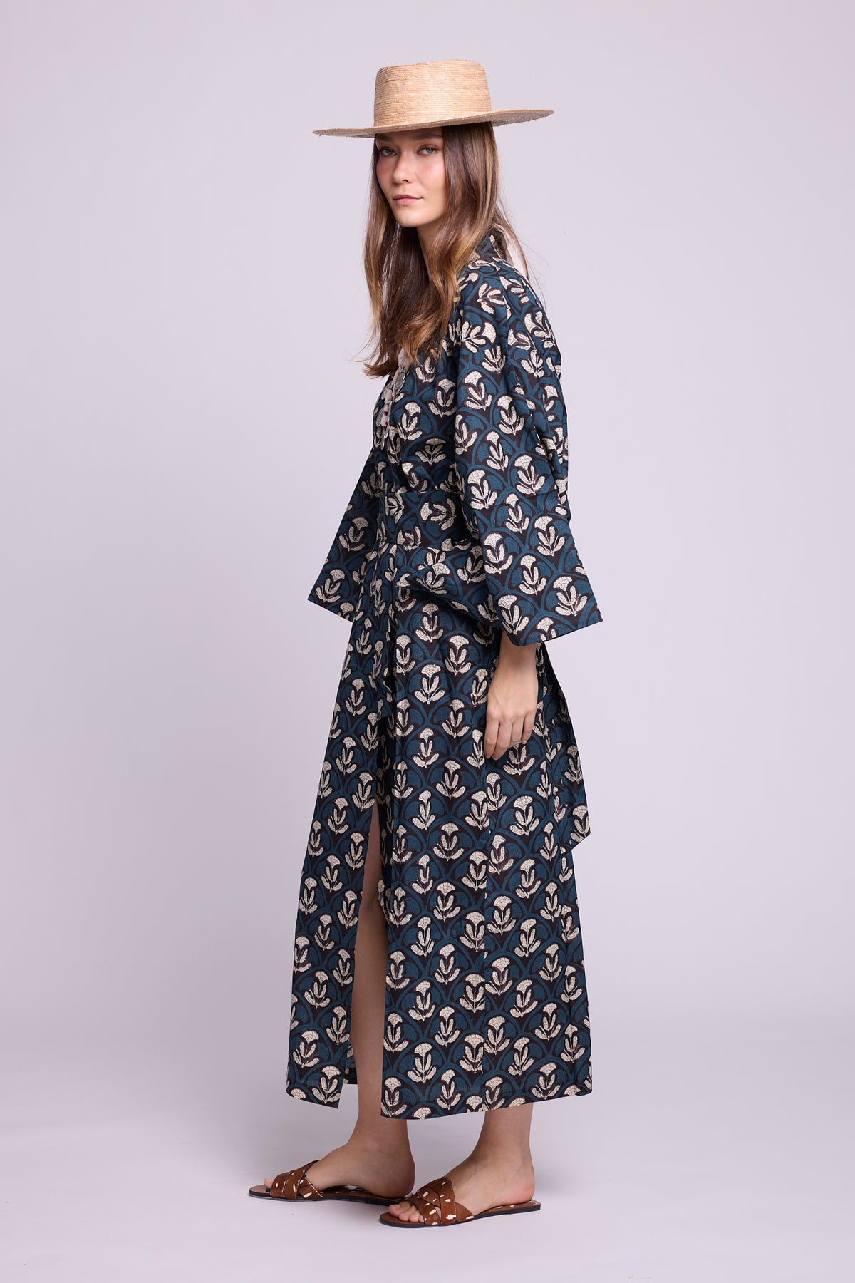 Side view of Kleed's krisant naya kimono. 100% cotton, hnadblockprinted flower motifs in blue and white. Model wearing a straw had and animal print caramel sandals.