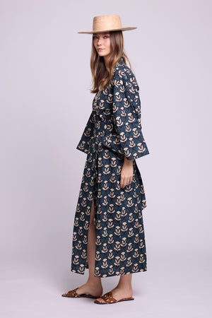 Side view of Kleed's krisant naya kimono. 100% cotton, hnadblockprinted flower motifs in blue and white. Model wearing a straw had and animal print caramel sandals.