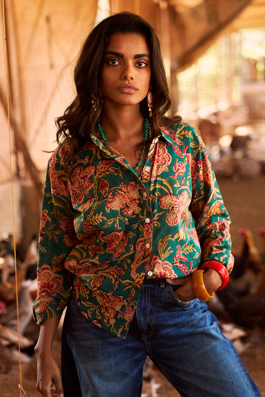 Model wearing the KLEED Lotus Green Shirt in 100% cotton, hand block printed with multicolour floral motifs and mother-of-pearl buttons, styled with blue denim and statement jewellery.