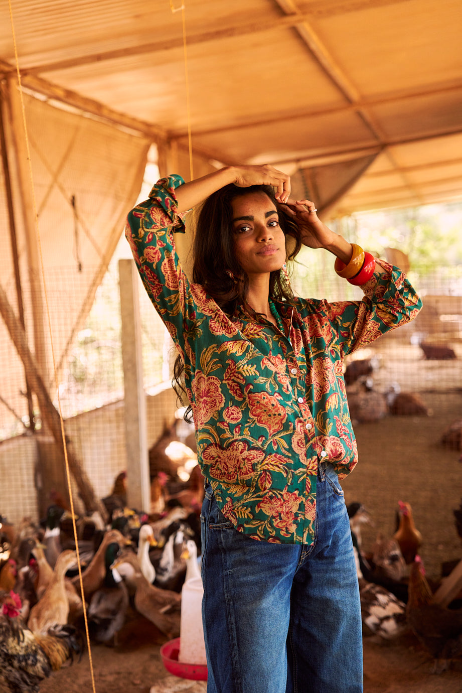 Model wearing the KLEED Lotus Green Shirt in 100% cotton, hand block printed with multicolour floral motifs and mother-of-pearl buttons, styled with blue denim in a relaxed artisanal setting.