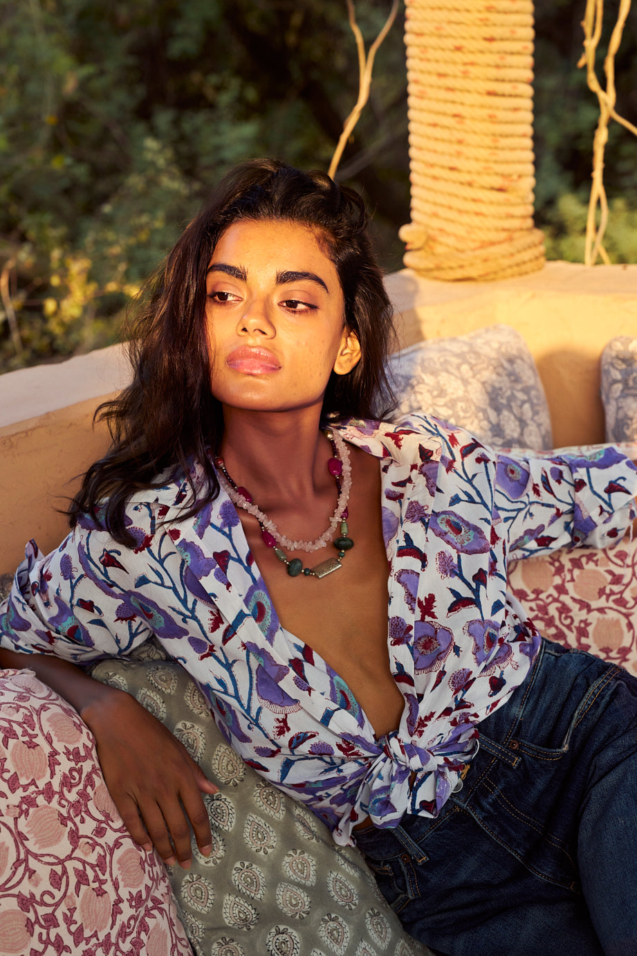 Model wearing the KLEED Lotus White Shirt in 100% cotton, hand block printed with lilac, blue, turquoise and burgundy floral motifs, styled tied at the waist with dark blue denim.