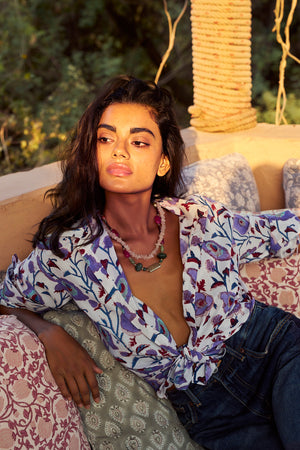 Model wearing the KLEED Lotus White Shirt in 100% cotton, hand block printed with lilac, blue, turquoise and burgundy floral motifs, styled tied at the waist with dark blue denim.