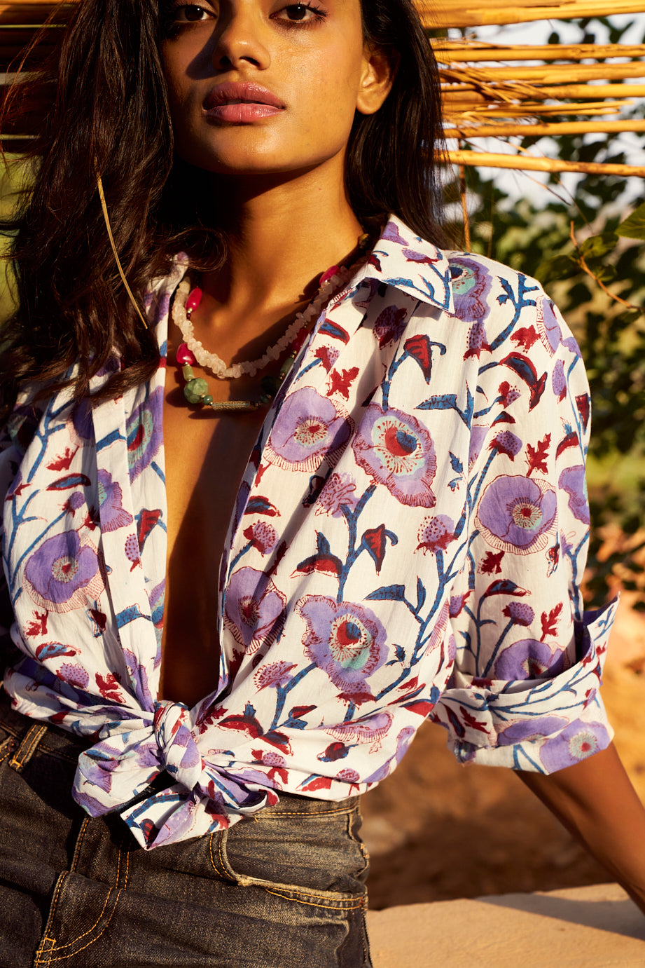 Model wearing the KLEED Lotus White Shirt in 100% cotton, hand block printed with lilac, blue, turquoise and burgundy floral motifs, styled open and tied at the waist with dark denim.
