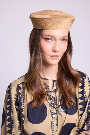 A woman wearing a woven tan beret-style hat and a beige patternedkleed shirt the midnight geo balloon shirt, in 100% cotton, with dark navy geometric motifs, photographed against a light gray studio background.