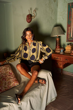 Woman sitting wearing Kleed Midnight Geo Balloon Shirt, a navy and sand geometric print cotton shirt with balloon sleeves, styled with black shorts