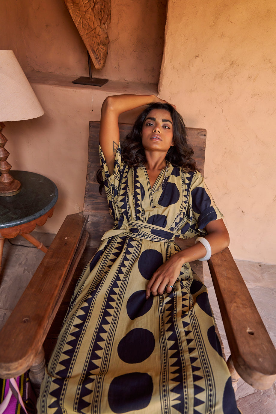 Model seated in a chair wearing midnight geo kaftan by kleed in 100% cotton, with geometric pattern in dark blue in beije base.
