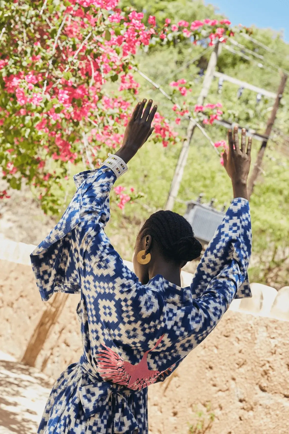 Woman wearing Kleed Mombasa Blue Kimono in handwoven Ikat cotton blue and white geometric pattern arms raised outdoor among flowers