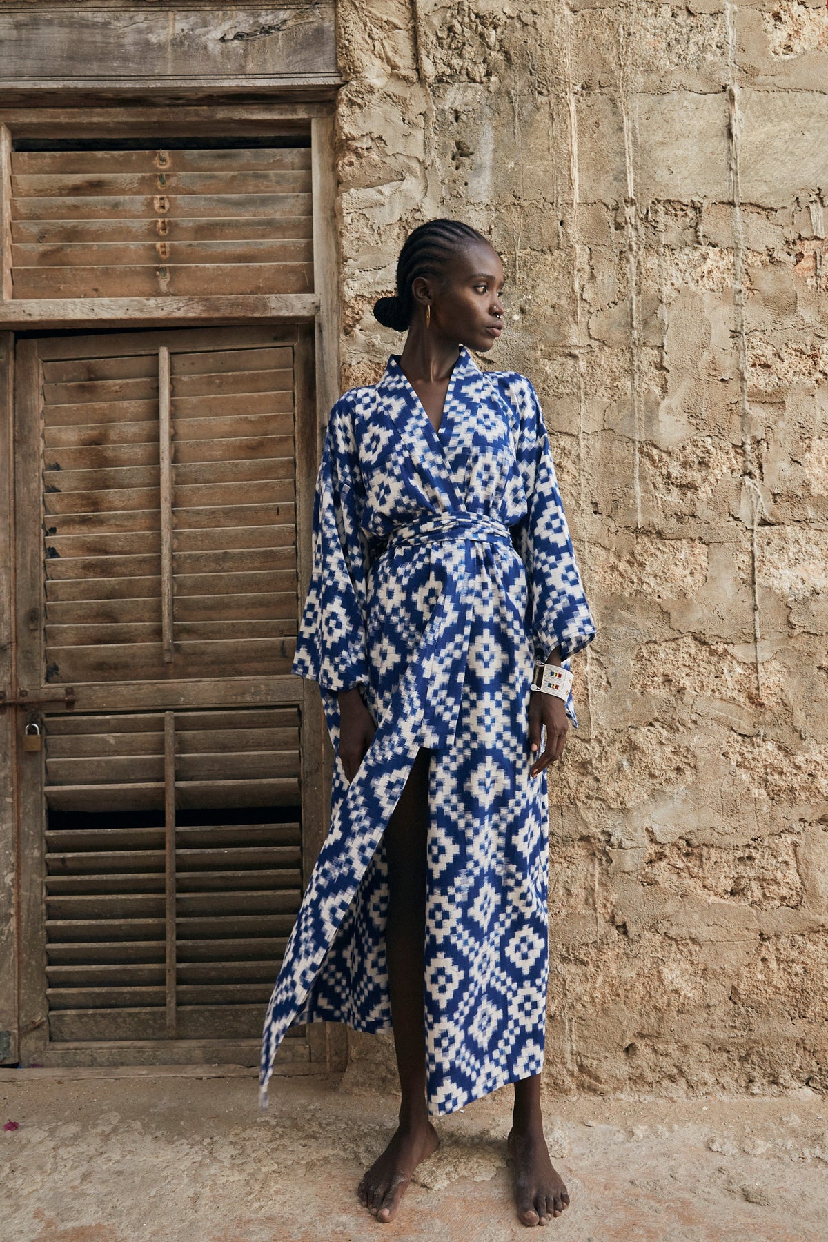 Woman wearing Kleed Mombasa Blue Kimono in handwoven Ikat cotton blue and white geometric pattern standing in doorway outdoor editorial