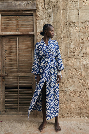 Woman wearing Kleed Mombasa Blue Kimono in handwoven Ikat cotton blue and white geometric pattern standing in doorway outdoor editorial
