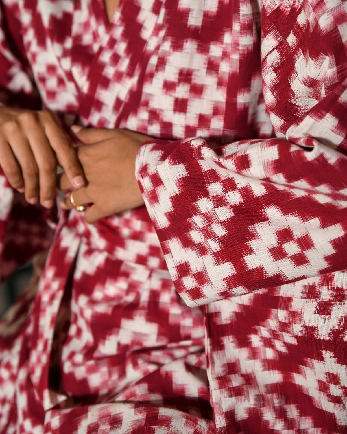 Close-up detail of Mombasa red Ikat woven cotton kimono by Kleed showing fabric texture and gold ring, handcrafted artisan loungewear