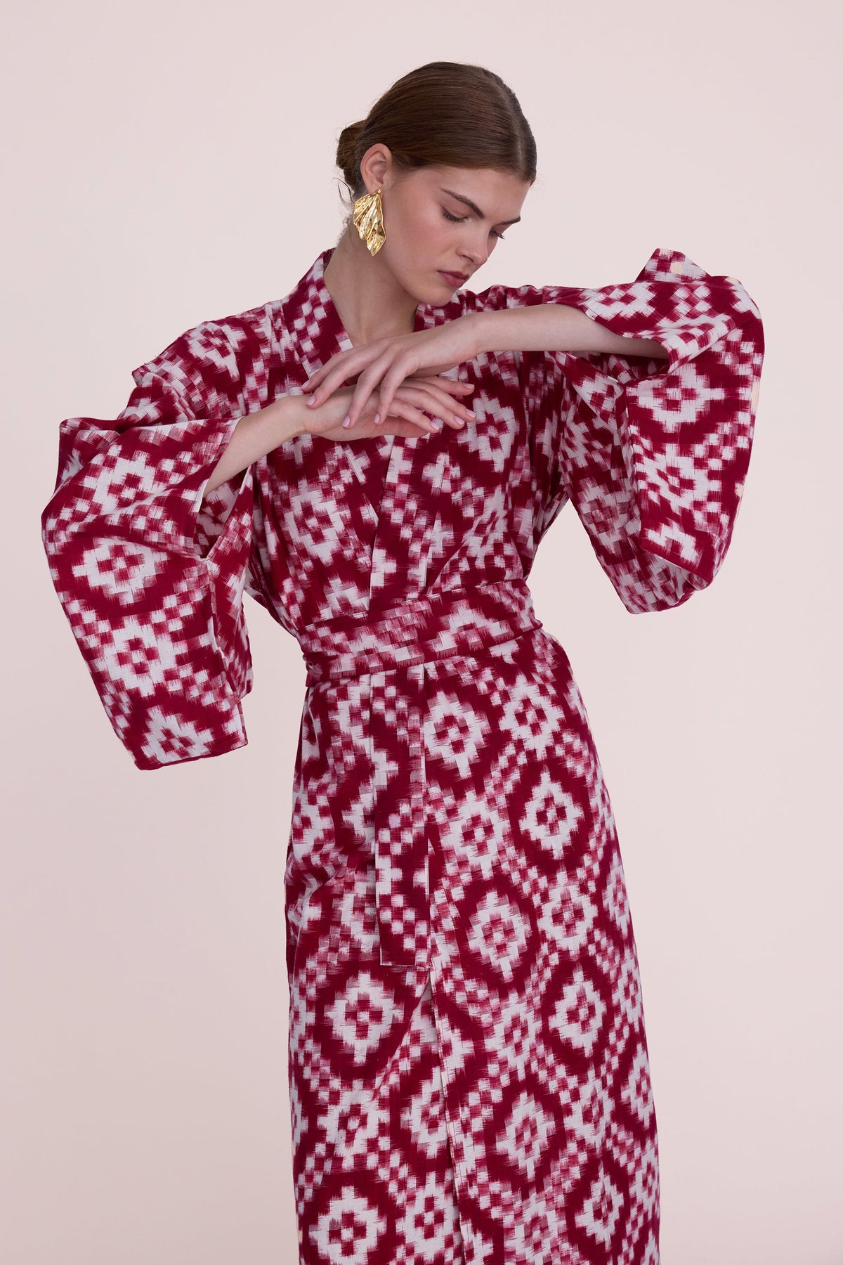 Woman wearing Mombasa red Ikat cotton kimono by Kleed, close-up detail of wide dramatic sleeves with gold leaf earrings, handcrafted sustainable loungewear