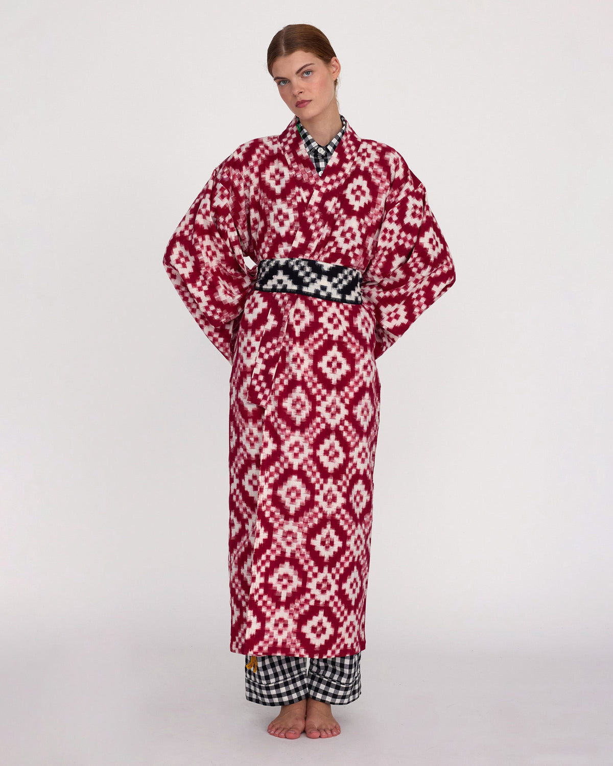 Front side of the Mombasa red Ikat cotton kimono by Kleed styled with black and white gingham belt and trousers, full length studio shot, handcrafted sustainable loungewear
