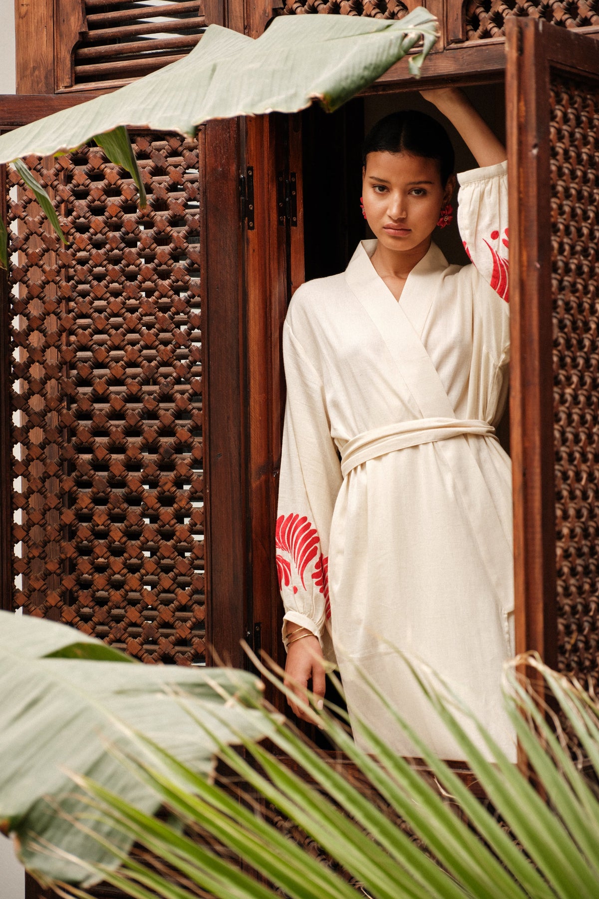Woman wearing Kleed Natural Kandy Kimono in 100% cotton ivory white with red floral hand embroidery on balloon sleeve cuffs standing in doorway