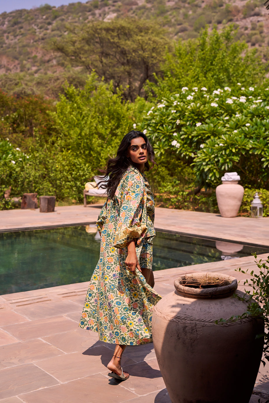 Model wearing the Kleed Palash Kimono outdoors on the pool side, hand blockprinted cotton kimono in cream with botanical flower pattern.