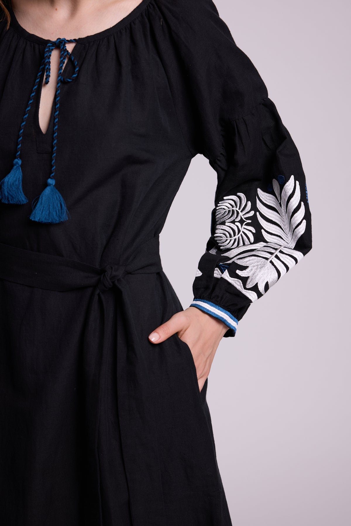 Close-up of the KLEED Portofino Black Kaftan showing the waist, sleeve embroidery and blue tassel detail.