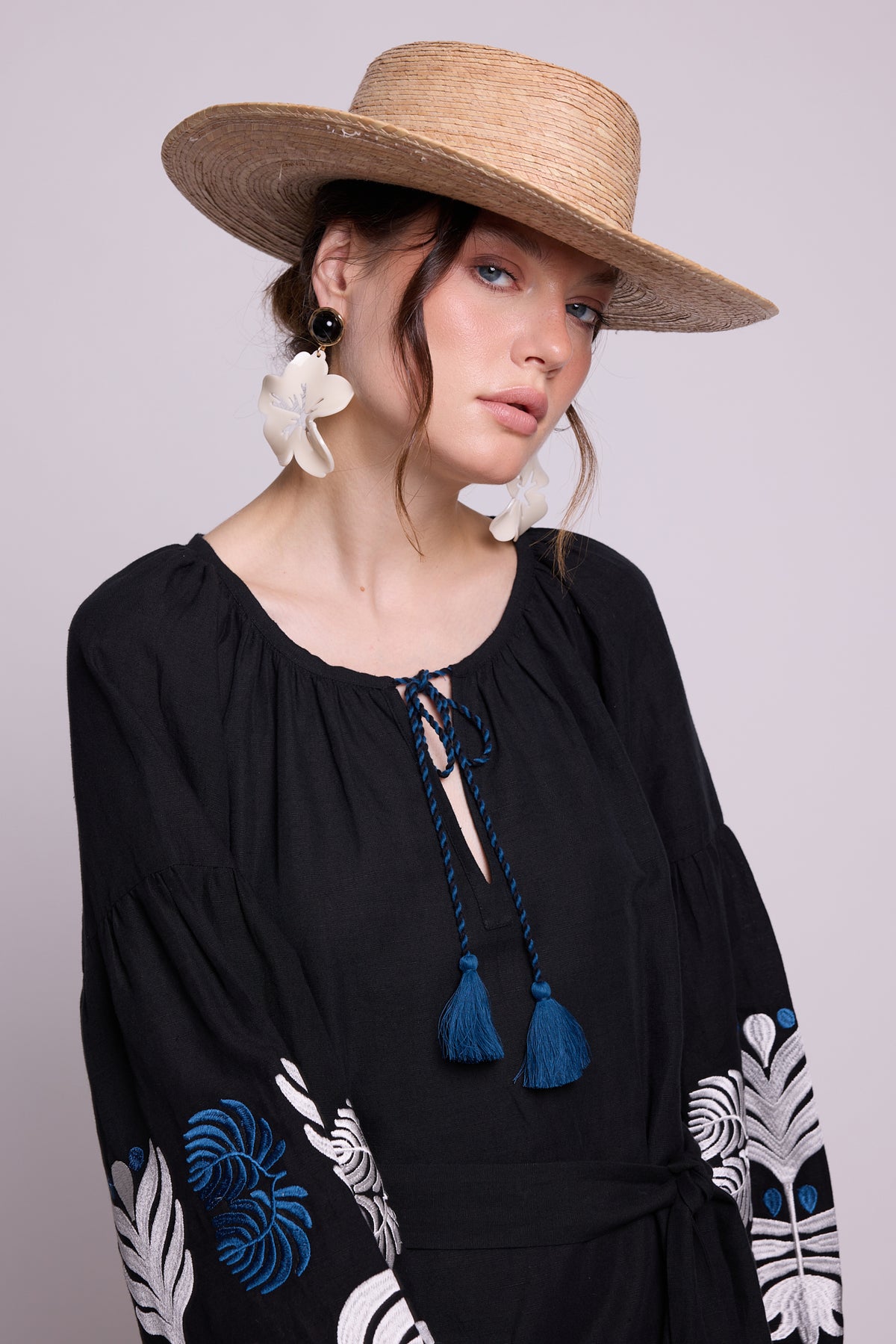 Portrait detail of model wearing the KLEED Portofino Black Kaftan with blue tassels and embroidered sleeves.