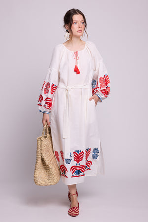 Model seated wearing the KLEED Portofino Black Kaftan with white embroidered details, blue tassels and a woven straw bag.