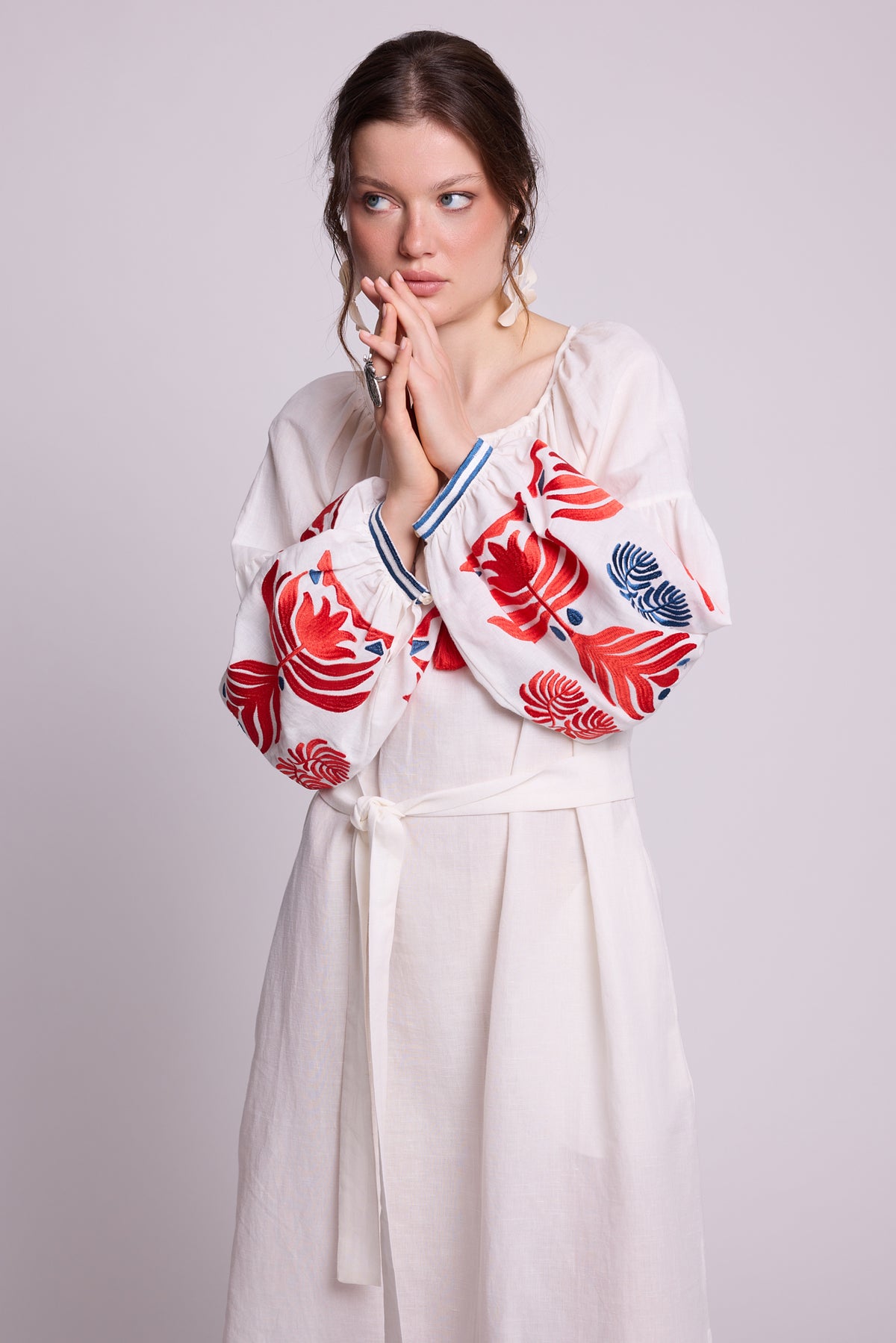 Close-up of model wearing the KLEED Portofino White Kaftan in cotton linen, showing the red tassel neckline, red and blue embroidered sleeves and statement earrings.