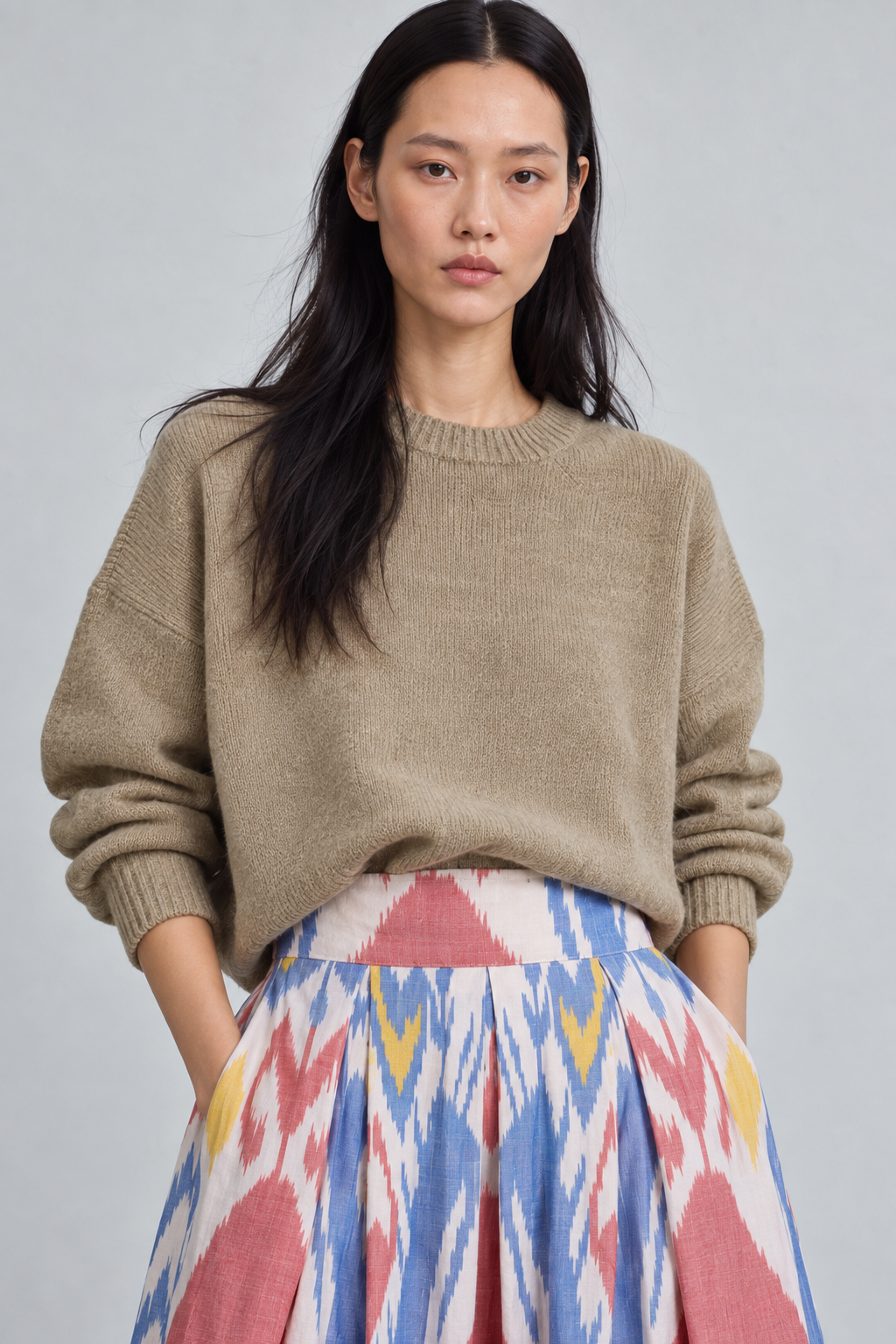 Model wearing the KLEED Seashore Skirt, artisan women’s ikat skirt in 100% hand-loomed cotton, featuring a colourful pleated midi silhouette and styled with a neutral knit sweater.
