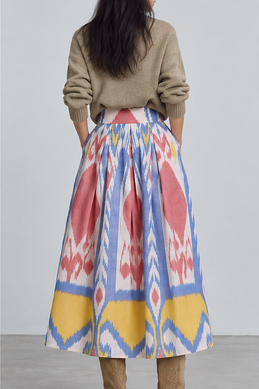 Back view of model wearing the KLEED Seashore Skirt, a women’s ikat midi skirt in 100% hand-loomed cotton with pleated volume, styled with a neutral knit sweater and tan boots.