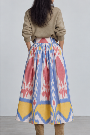 Back view of model wearing the KLEED Seashore Skirt, a women’s ikat midi skirt in 100% hand-loomed cotton with pleated volume, styled with a neutral knit sweater and tan boots.